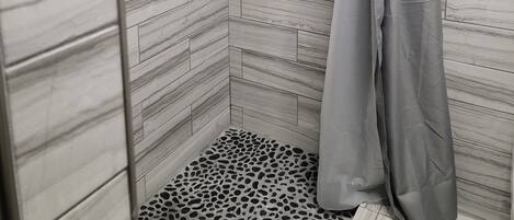A shower with a grey curtain and a patterned floor.