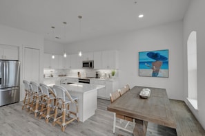 A modern kitchen with white cabinetry, a central island with seating, stainless steel appliances, and pendant lighting.