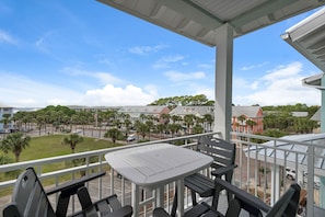 A balcony with a table and chairs, overlooking a parking lot and buildings with palm trees.