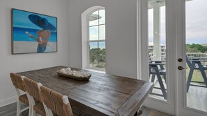 A dining area with a wooden table, white chairs, and a painting of a beach scene. - GULF PLACE-STUNNING CONDO OFF 30A!! 3 BED/3 BATH!! SLEEPS 6!! (Santa Rosa Beach)