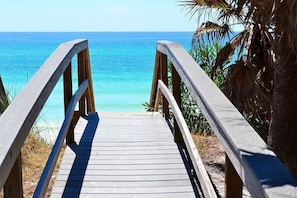 Une promenade en bois qui mène à une plage aux eaux d’un bleu limpide.