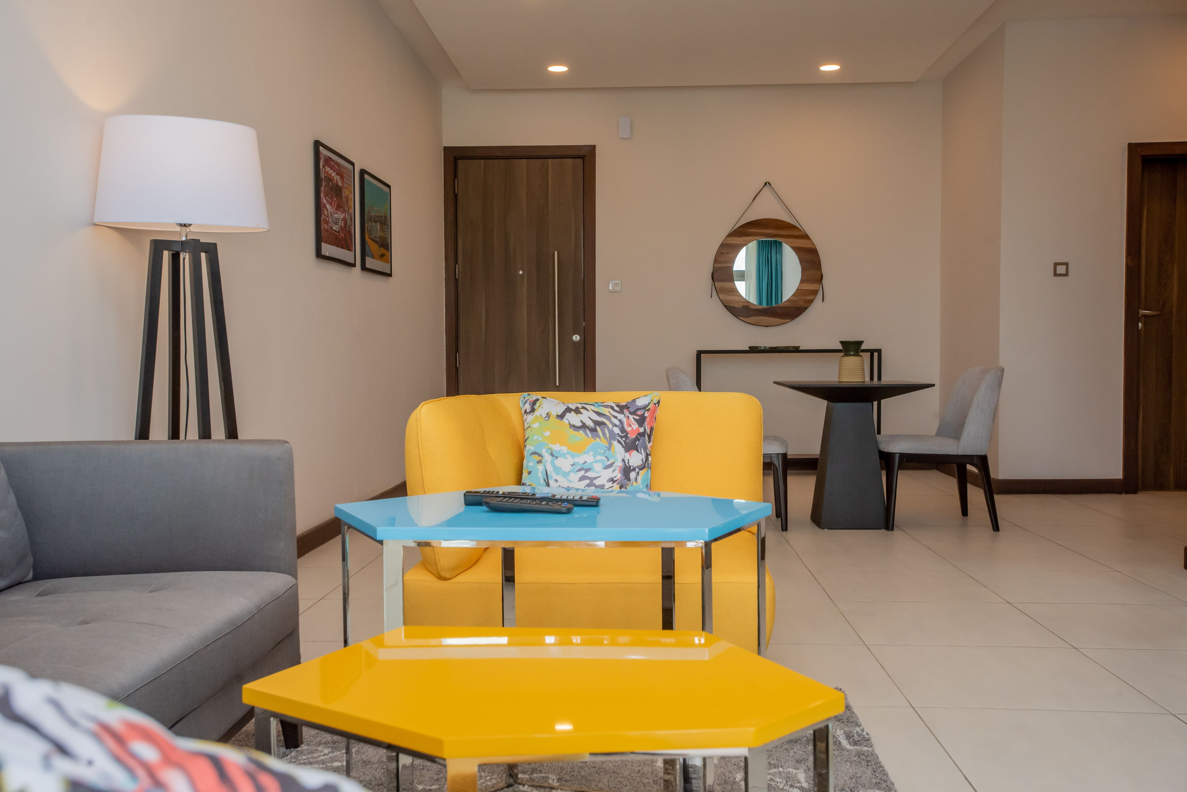 Una sala de estar moderna con un sofá, un sillón amarillo, una mesita, una lámpara y un espejo en la pared.