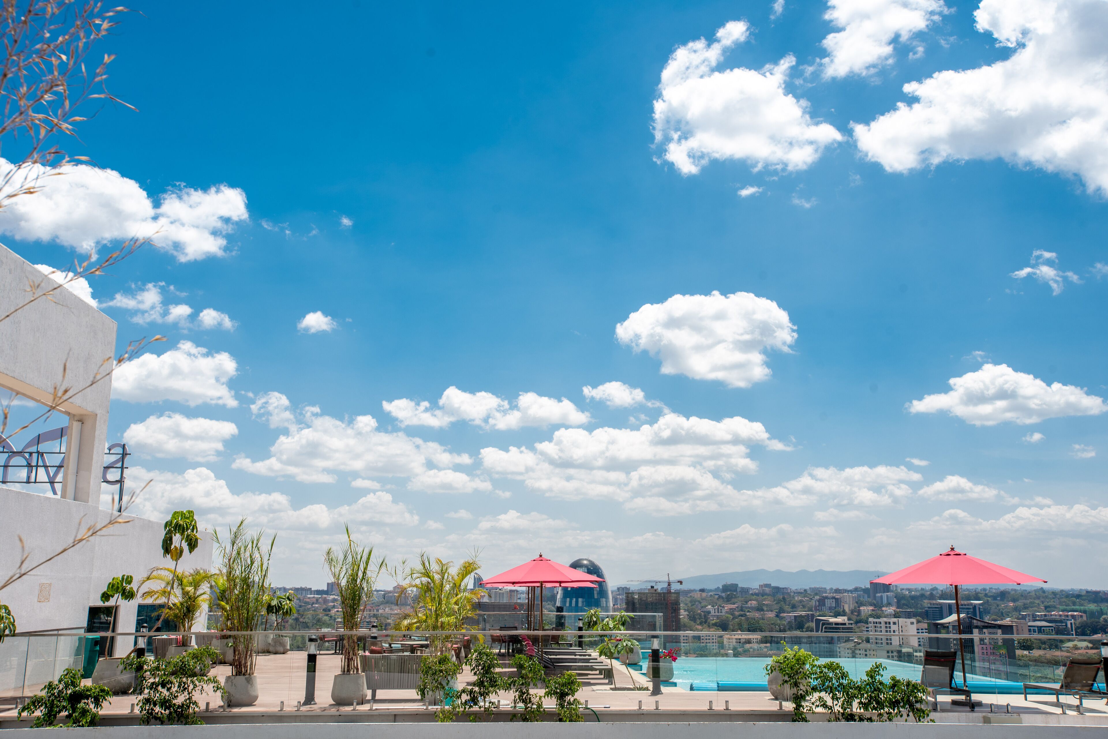 Zona de piscina en la azotea con sillones de descanso y sombrillas, con vistas a un paisaje urbano y montañas.