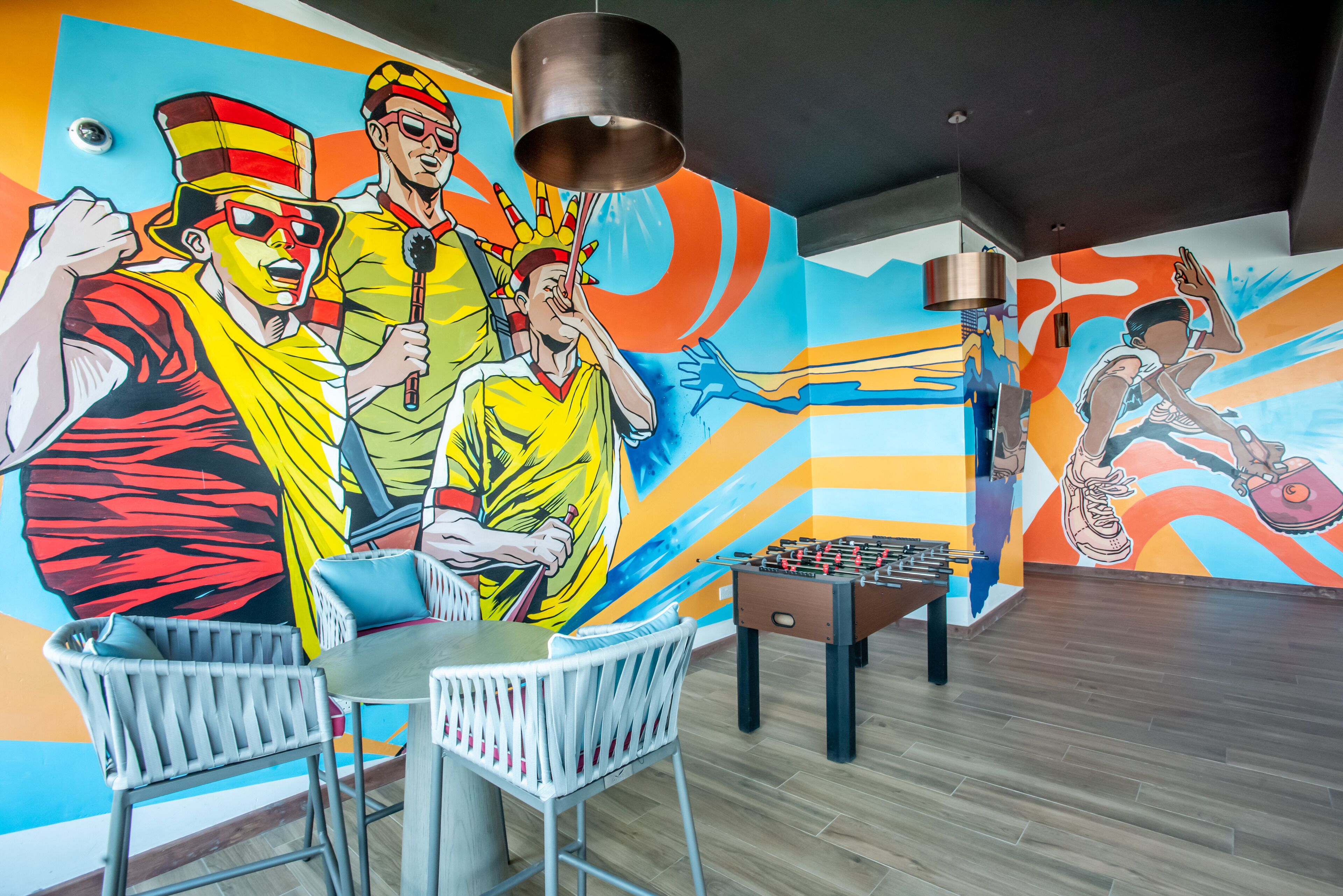 A room with a foosball table, a mural with colorful characters, and a table with chairs.