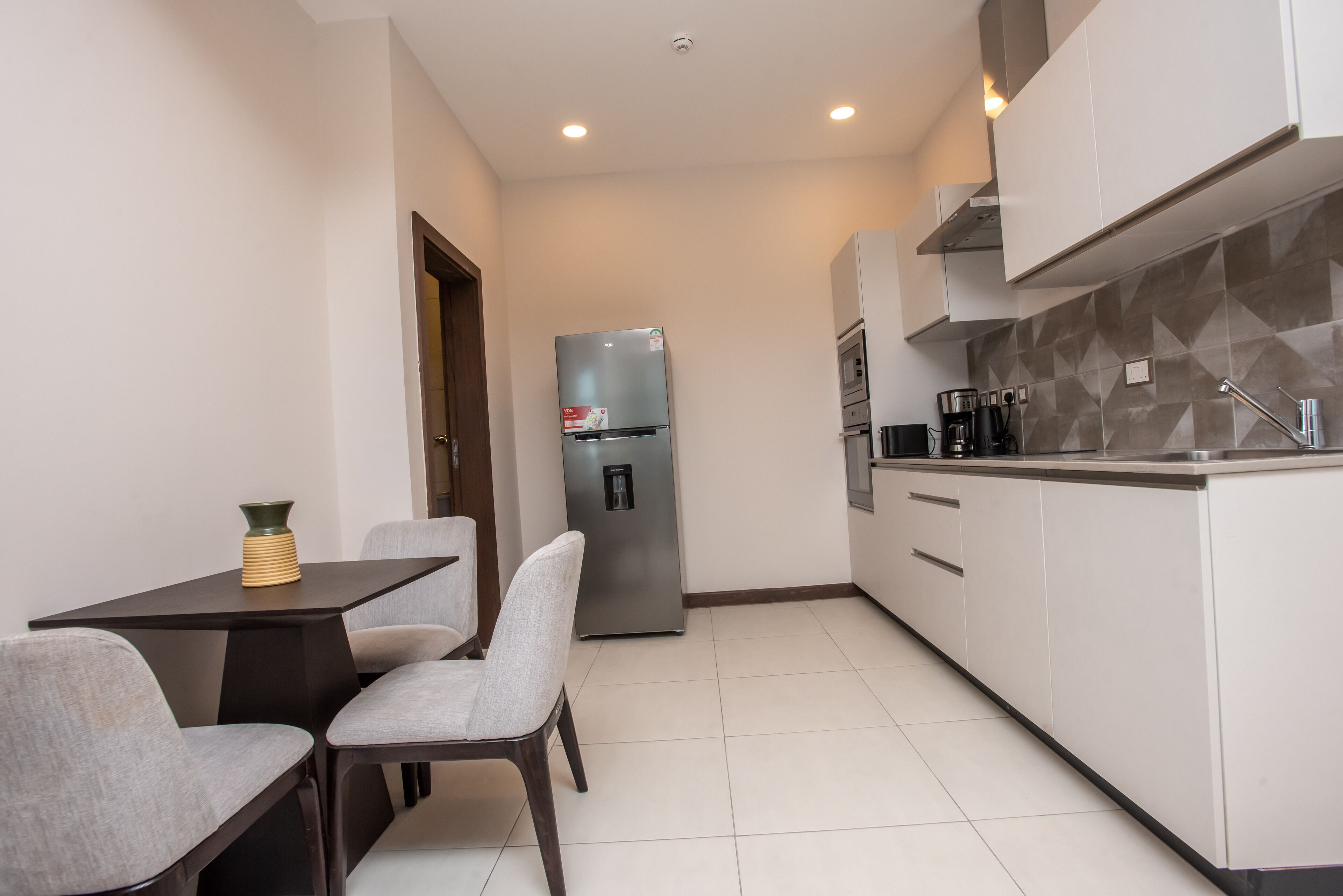 Una cocina moderna con refrigerador integrado, comedor con mesa y sillas, y salpicadero de azulejos.