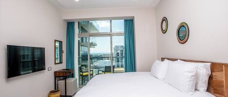 A hotel room with a large bed, a flat-screen TV, a sliding glass door to a balcony, and a city view.