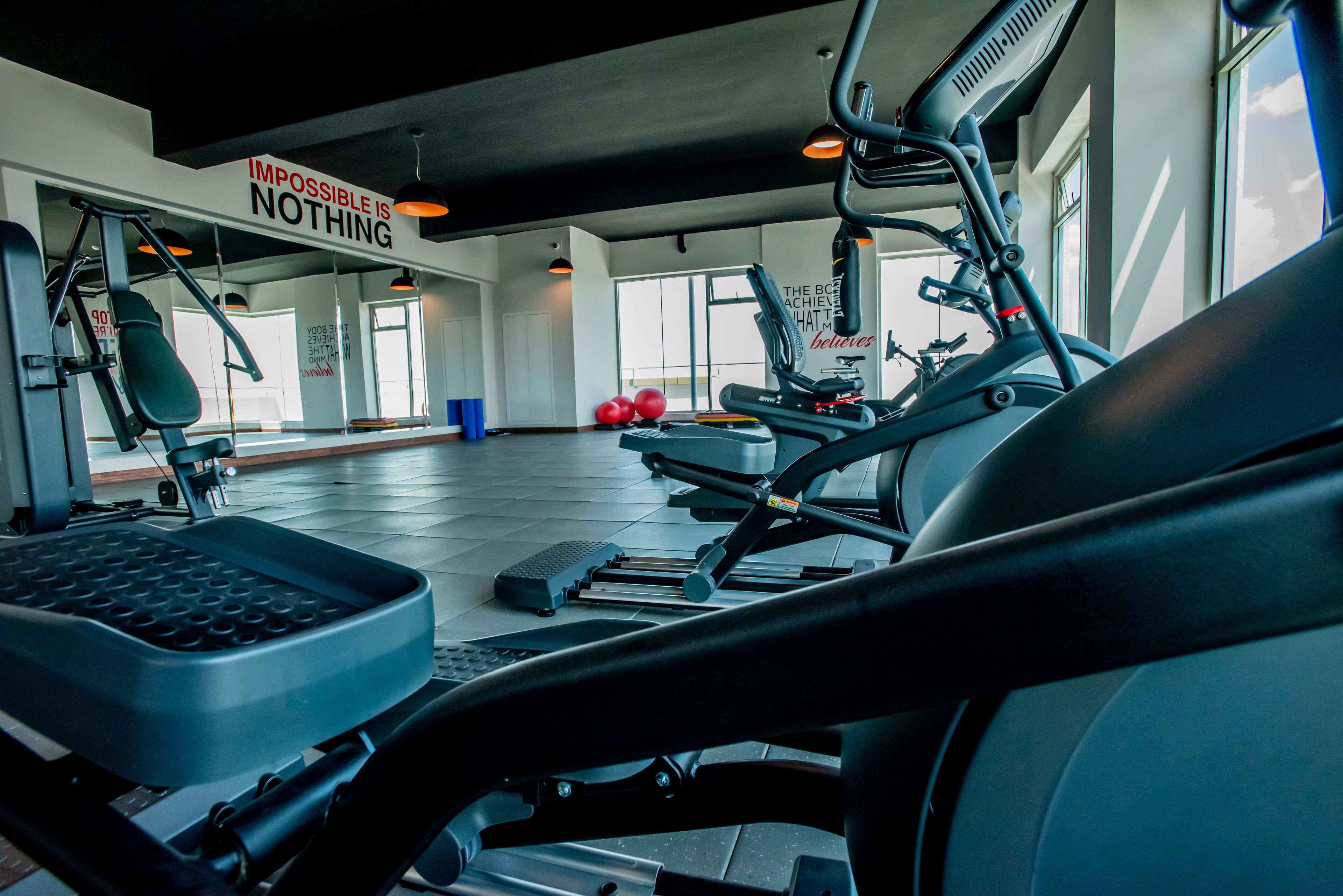 Une salle de sport équipée de matériel d’exercice, avec une affiche motivante et de grandes fenêtres.