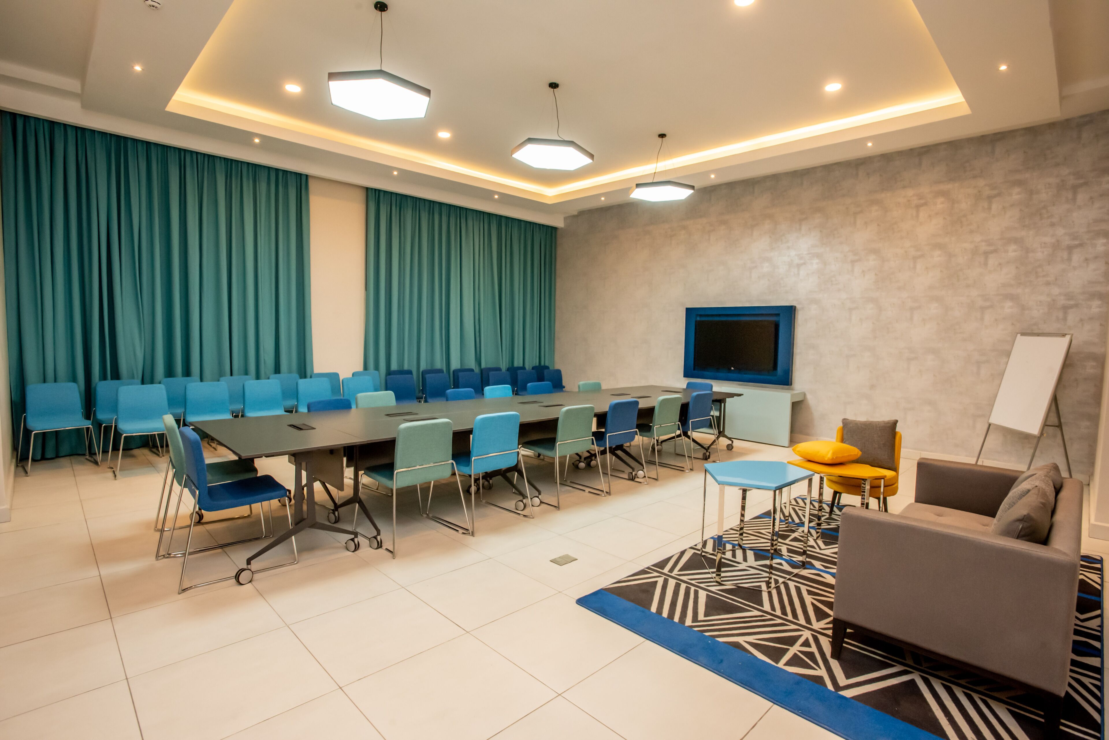 A conference room with a long table, blue chairs, a sofa, and a TV on the wall.