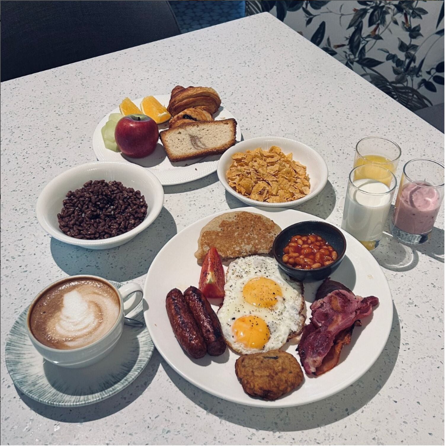 A breakfast plate with eggs, sausages, bacon, beans, toast, and a coffee cup.
