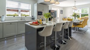 A modern kitchen with a central island, bar stools, and a dining area with yellow chairs. - Routhorpe House (Driffield)
