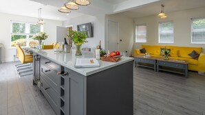A modern kitchen with a central island, a dining area with yellow chairs, and a living room with a yellow sofa. - Routhorpe House (Driffield)