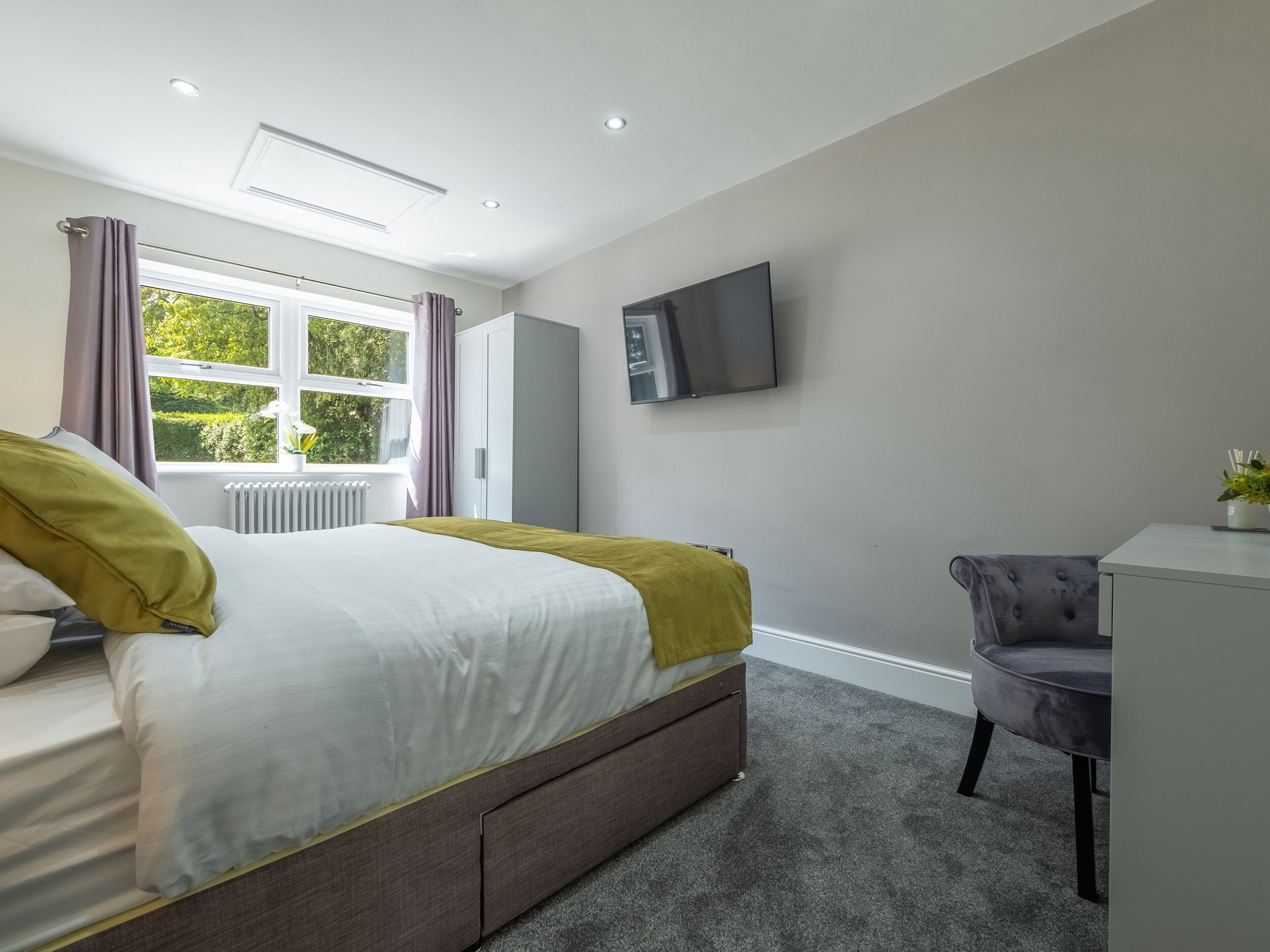 Une chambre à coucher moderne avec un lit, un bureau et un téléviseur fixé au mur.
