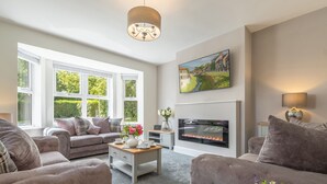 A modern living room with a fireplace, comfortable seating, and a large window offering a view of greenery. - Routhorpe House (Driffield)