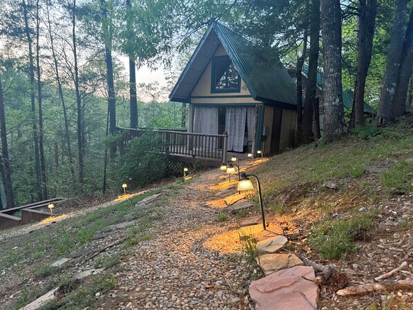 A cabin with a wooden deck, surrounded by trees.