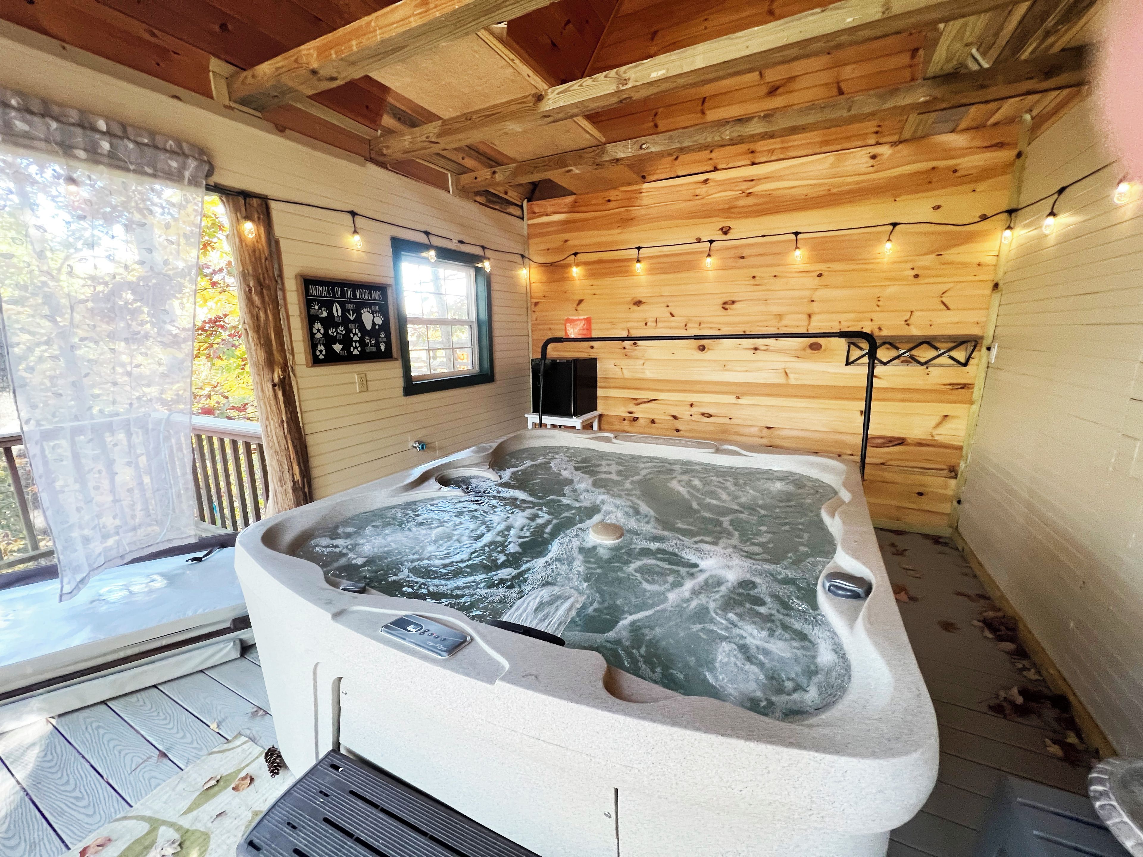 A hot tub in a wooden cabin with a window and string lights.
