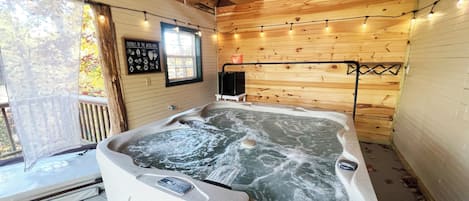 A hot tub in a wooden cabin with a window and string lights.