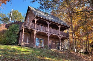 A wooden cabin with a balcony, surrounded by trees and a grassy yard.