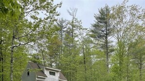 A two-story house with a porch, outdoor seating area with Adirondack chairs, and a picnic table.