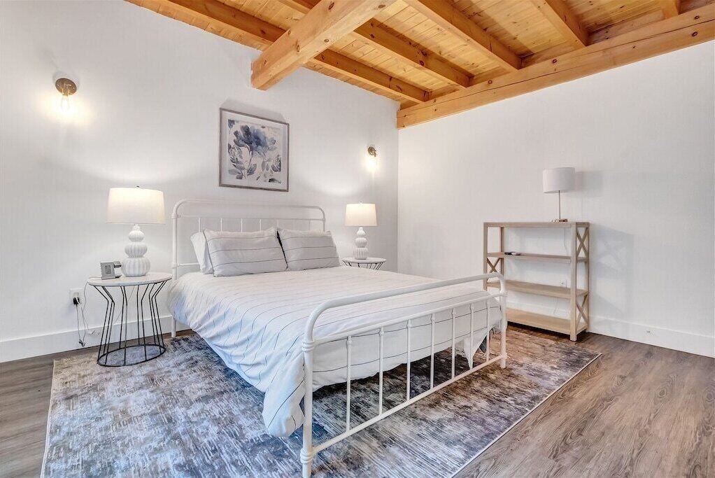 Ein Schlafzimmer mit einem Bett, Nachttischen, einer Lampe, einem gerahmten Bild und einem Holzregal.
