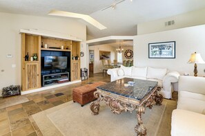 A spacious living room with a large TV, a white sofa, a coffee table, and a fireplace. - Indian Wells Oasis w/ Pool: Walk to Tennis Garden! (Indian Wells)