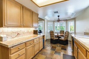 A kitchen with wooden cabinets, a granite countertop, a microwave, and a dining area with chairs and a table.
