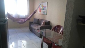 A living room with a glass table, a sofa, a hammock, and a painting on the wall.