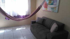 A living room with a gray sofa, a checkered hammock, and a colorful abstract painting on the wall. - APARTMENT NEAR SKYSURF CUMBUCO IN CAUCAIA (CAUCAIA)