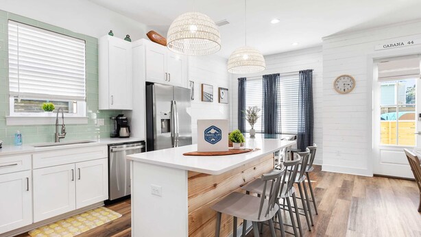 Una cocina moderna con armarios blancos, una isla central con taburetes, un refrigerador y un fregadero.