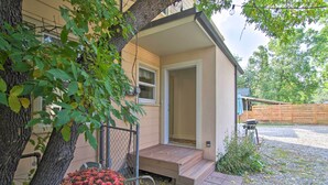 A small house with a wooden porch, a fenced yard, and a tree with green leaves. - Mid-Century Bozeman Townhome ~ 1 Mi to Dtwn! (Bozeman)