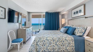 Een slaapkamer met een groot bed, een dressoir, een stoel en uitzicht op zee via een balkondeur.