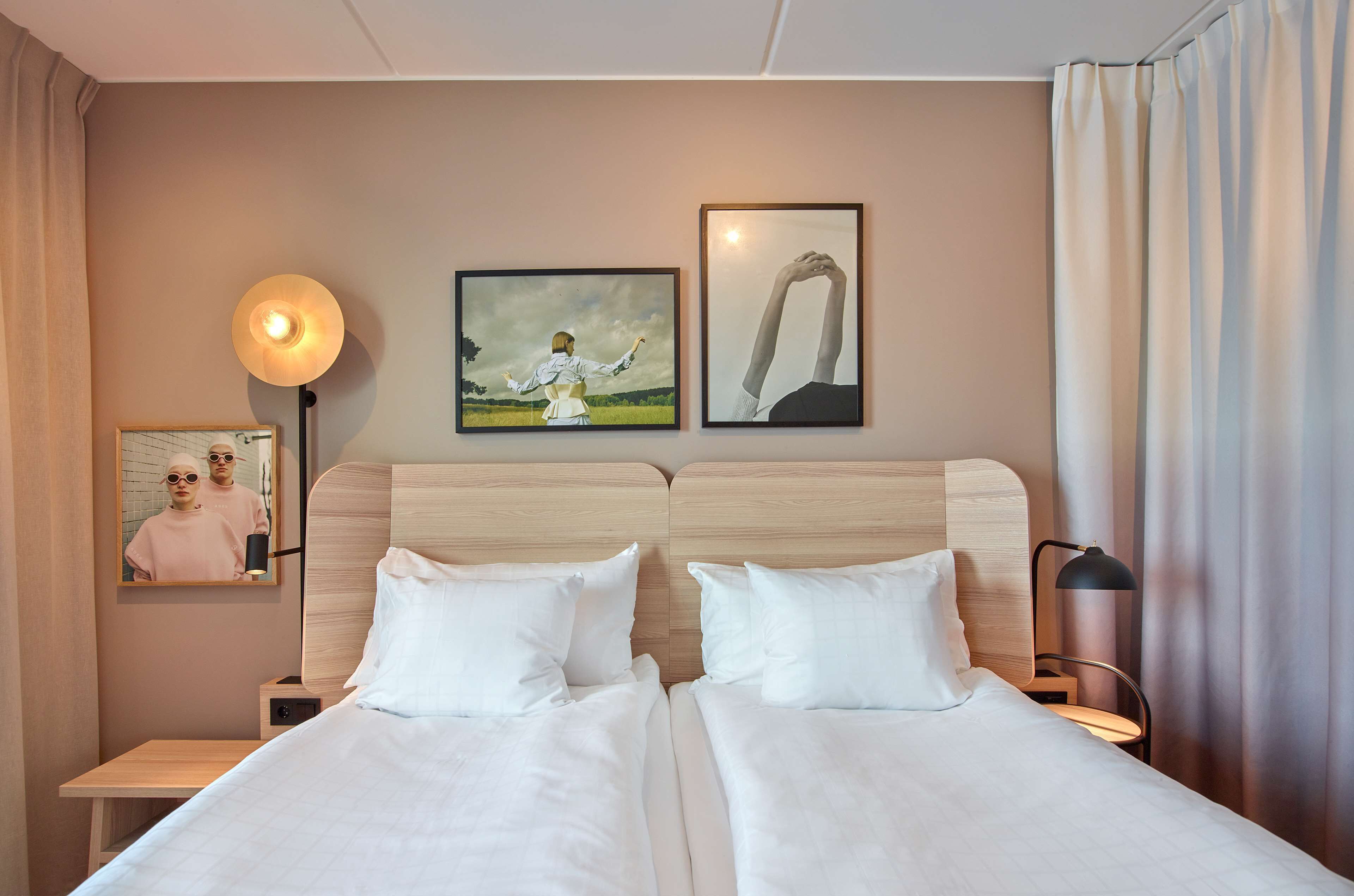 A hotel room with two beds, a bedside table, a lamp, and artwork on the wall.