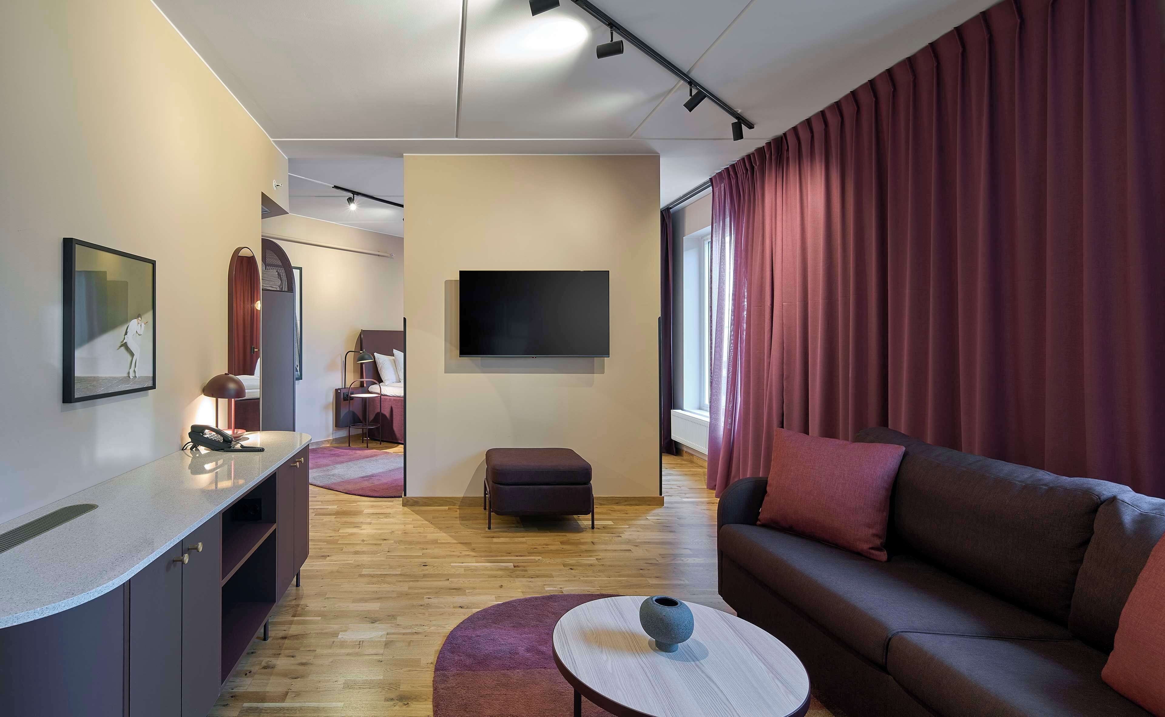 Una habitación de hotel moderna con sofá, una mesita, televisor y escritorio con teléfono.