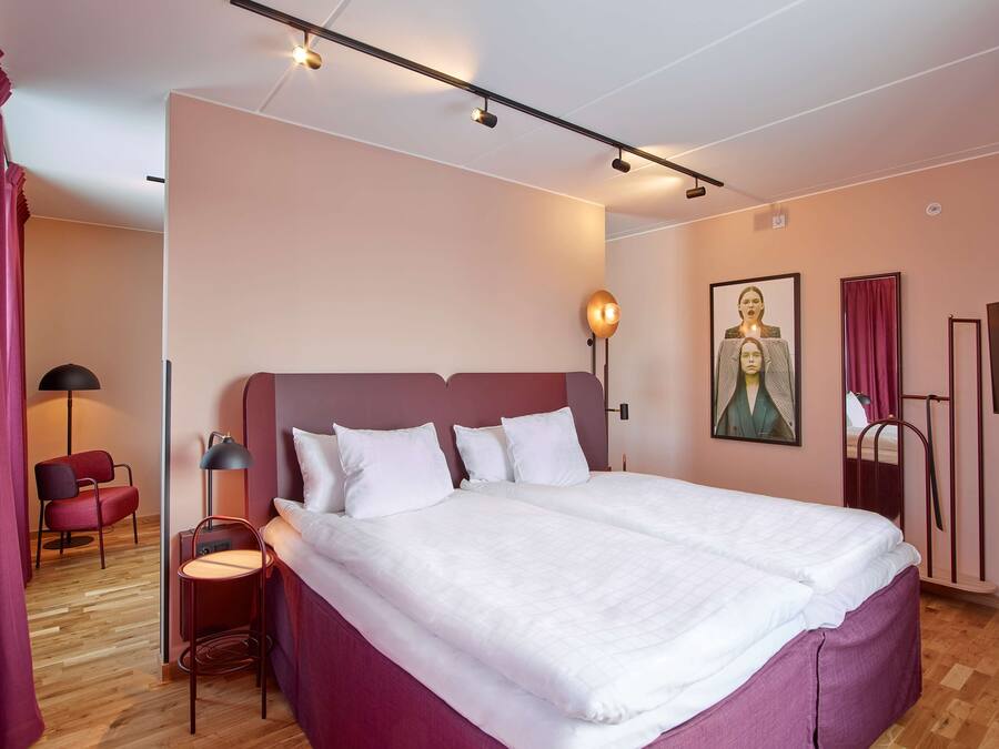 Ett modernt hotellrum med en stor säng, ett skrivbord, en stol och en lampa.