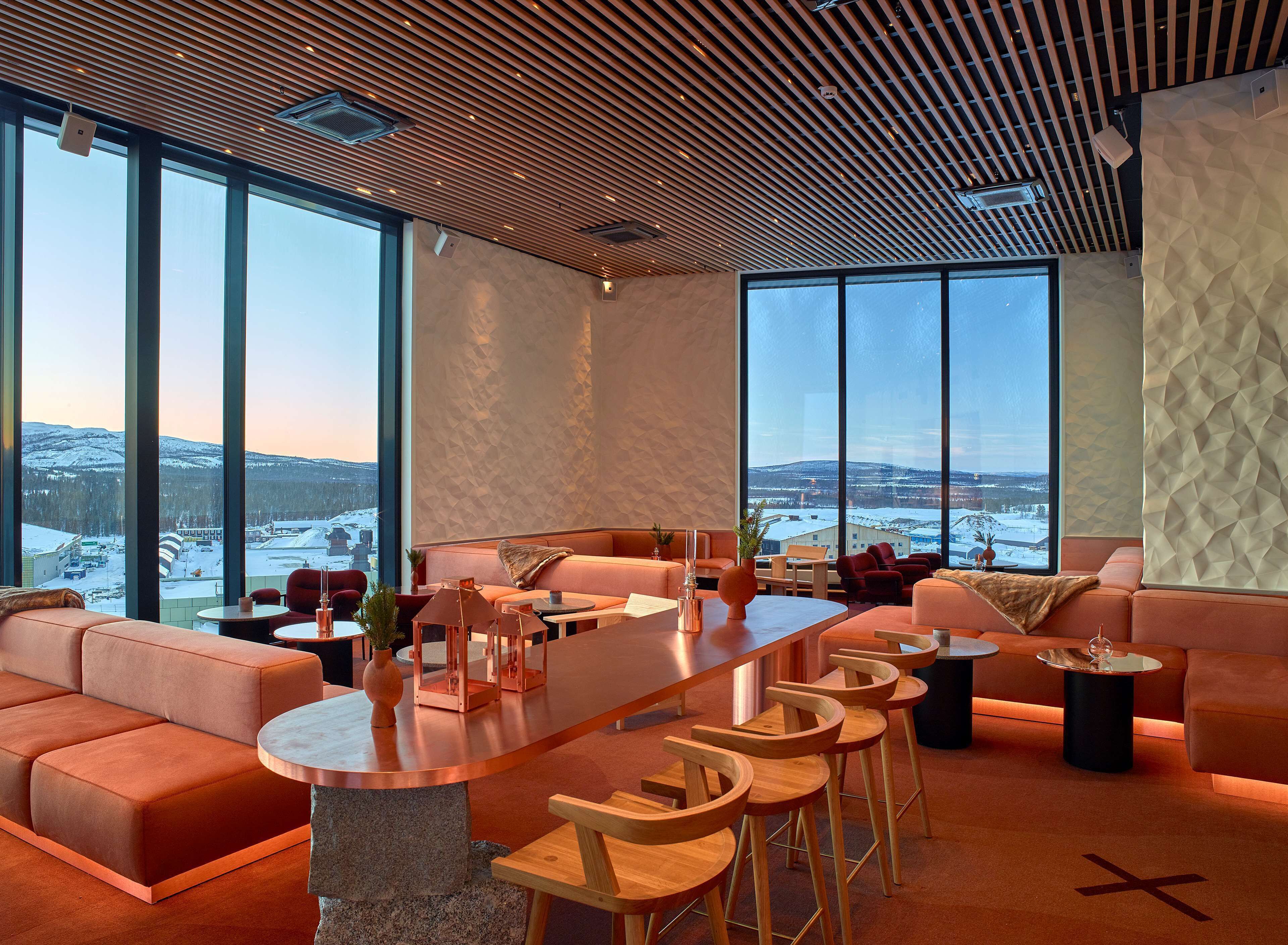 A modern interior with a large seating area, a bar, and large windows offering a view of a snowy landscape.