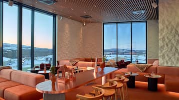Un interior moderno con una amplia zona de estar, un bar y grandes ventanales que ofrecen vistas a un paisaje nevado.