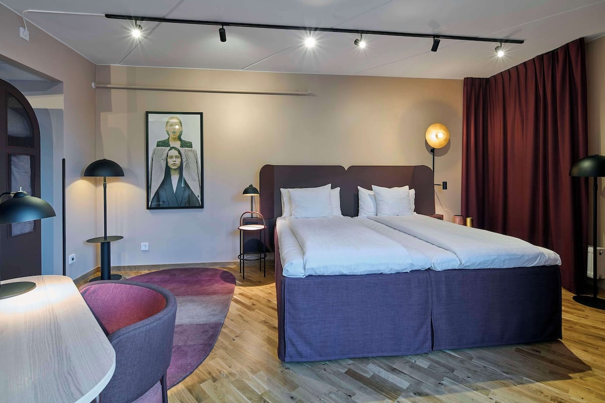 Une chambre d’hôtel moderne avec un grand lit, un bureau, une chaise et un tableau au mur.