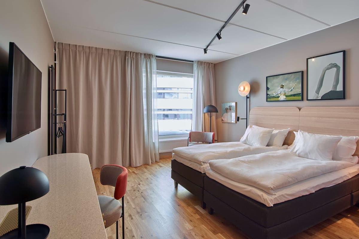 Une chambre d’hôtel avec deux lits, un bureau, une chaise, une télévision et une fenêtre avec des rideaux.