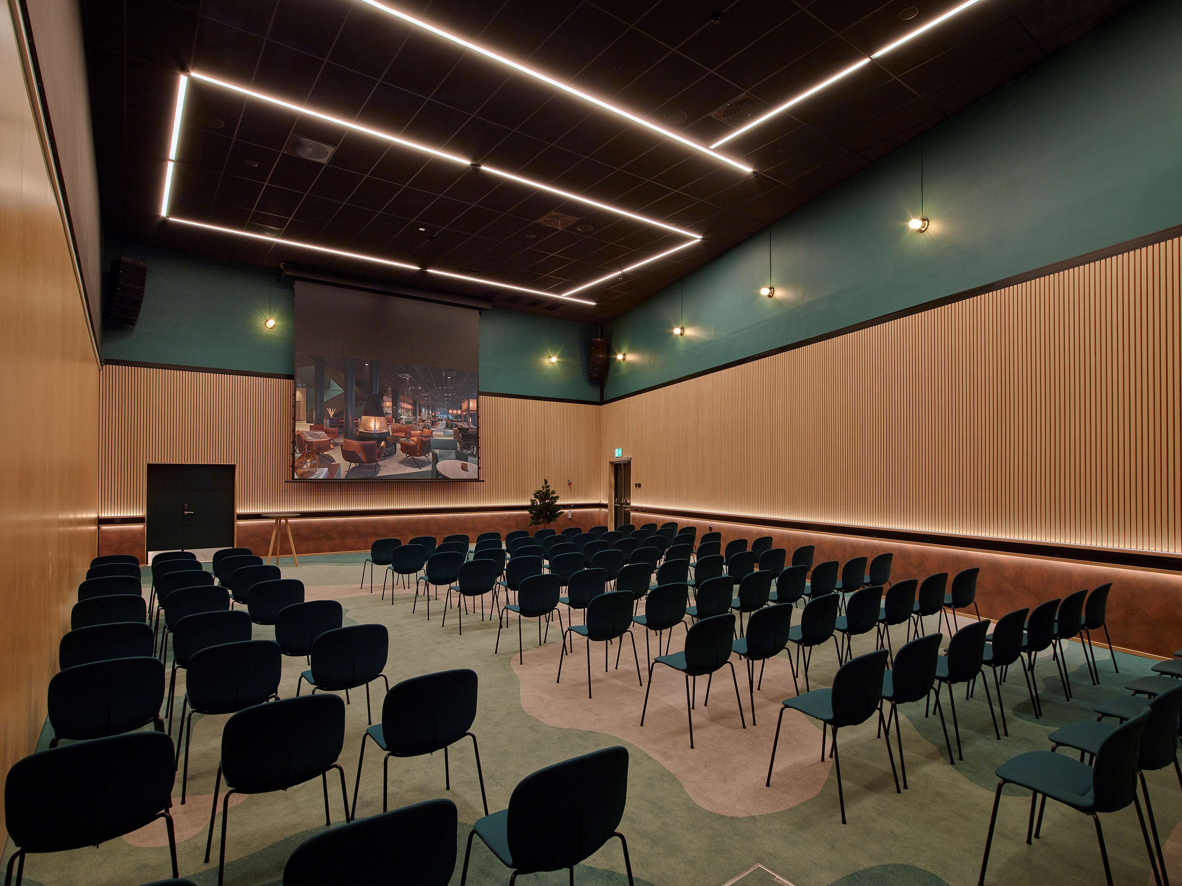 A conference room with rows of chairs, a large screen, and a stage.
