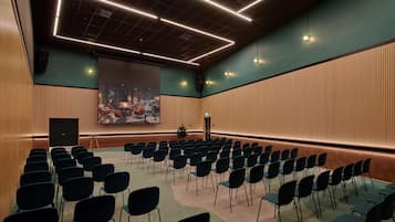 A conference room with rows of chairs, a large screen, and a stage.
