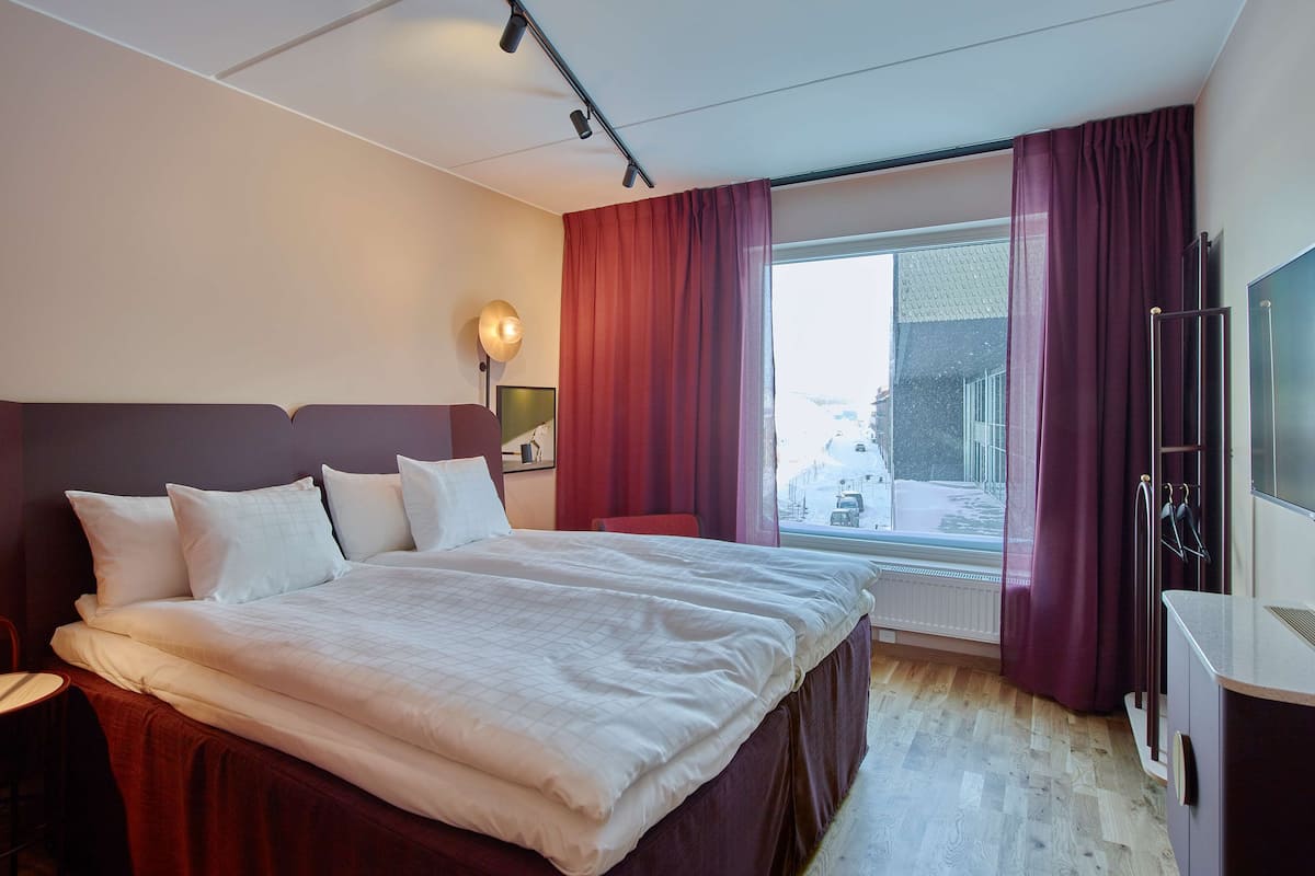 Une chambre d’hôtel avec un grand lit, un bureau, une télévision et une fenêtre avec des rideaux.