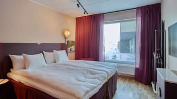 A hotel room with a large bed, a desk, a TV, and a window with curtains.