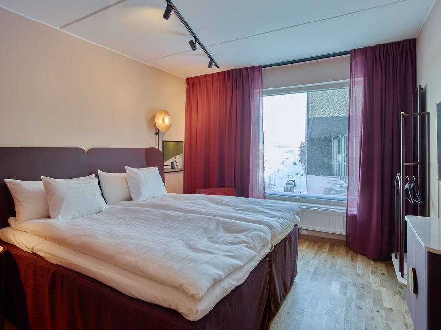 A hotel room with a large bed, a desk, a TV, and a window with curtains.
