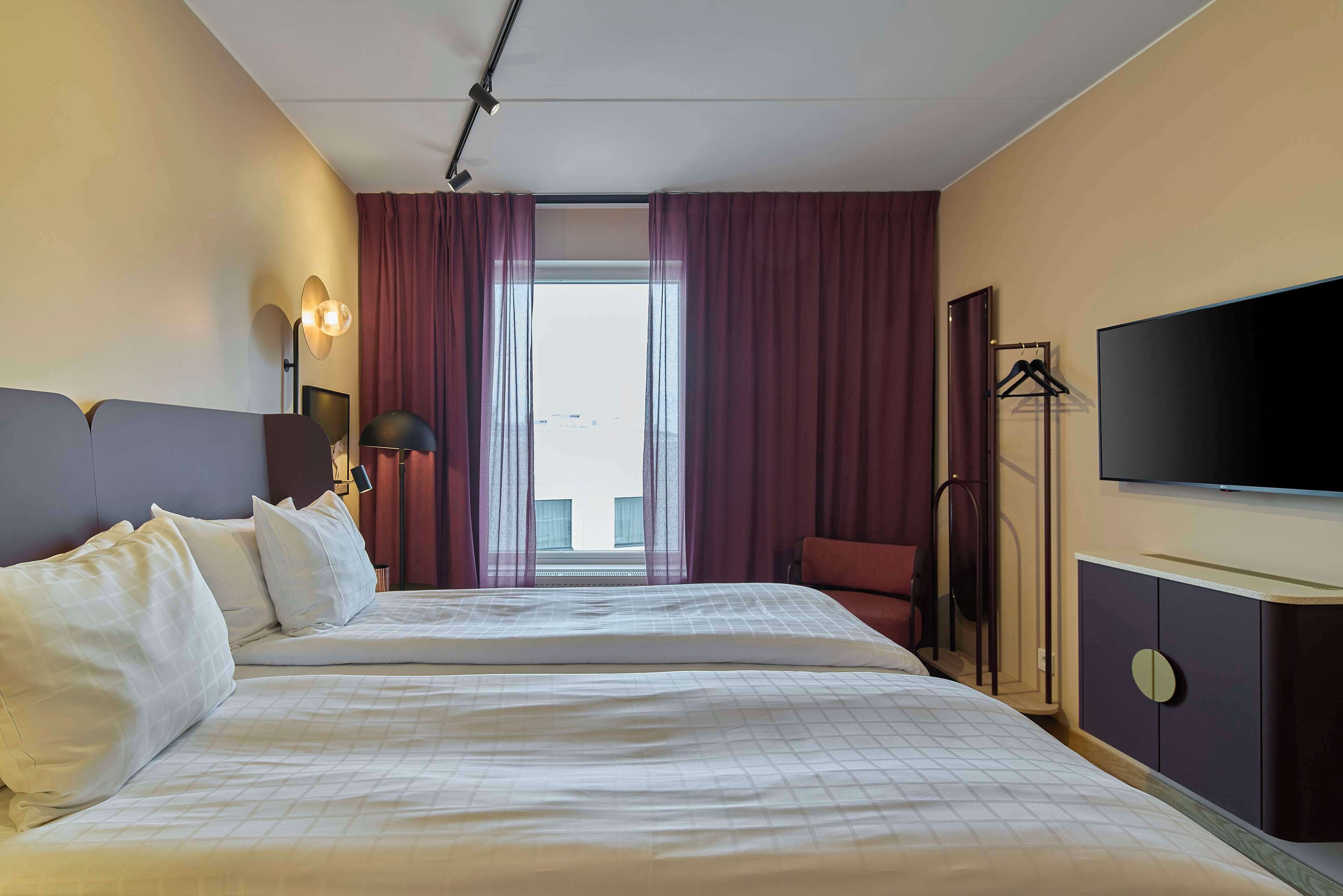 Una habitación de hotel con una cama grande, televisión, armario y ventana con cortinas.