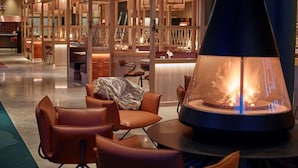 Un área de descanso moderna con asientos de cuero, una chimenea central y detalles de madera.