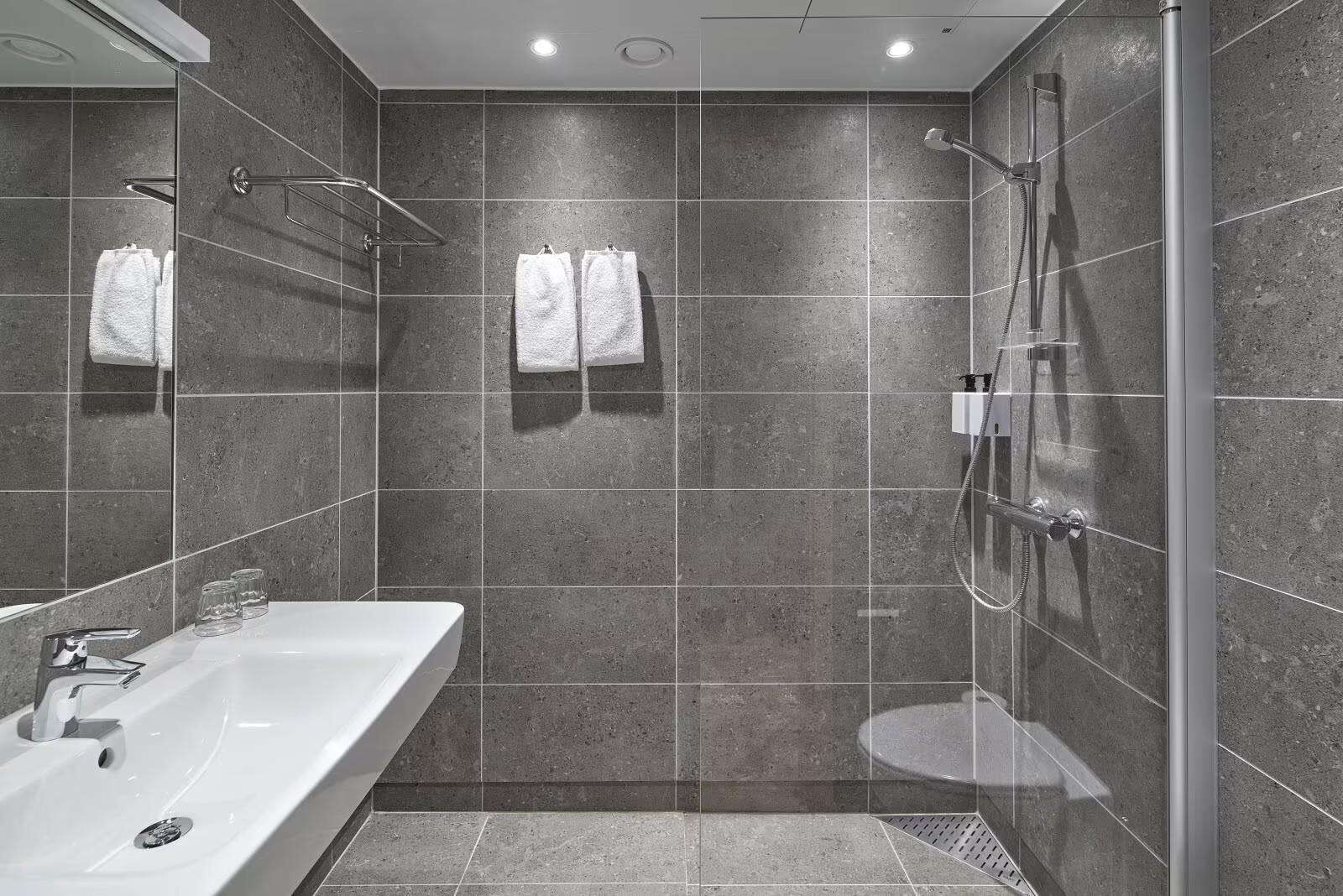 Un baño moderno con un lavamanos grande y blanco, una ducha con cerramiento de vidrio y dos toallas blancas colgadas en la pared.