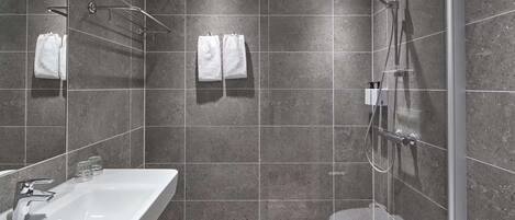 Un baño moderno con un lavamanos grande y blanco, una ducha con cerramiento de vidrio y dos toallas blancas colgadas en la pared.