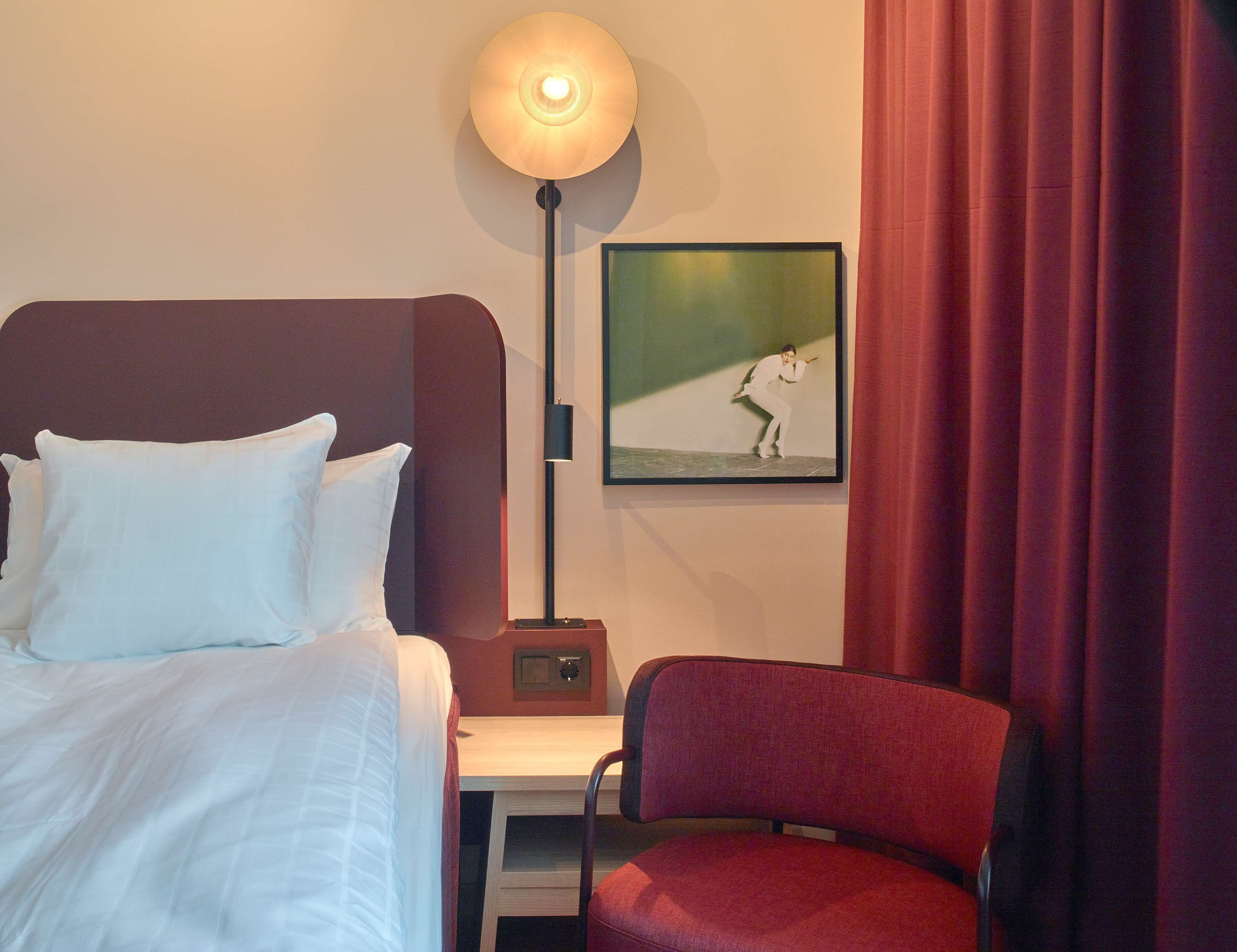 Een hotelkamer met een bed, een bureau, een stoel, een lamp en een lijst met een afbeelding aan de muur.