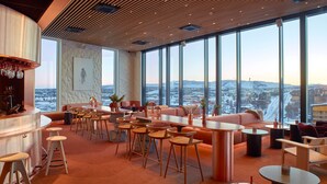 Un salón moderno con bar, zonas de estar y grandes ventanales con vistas a la ciudad.