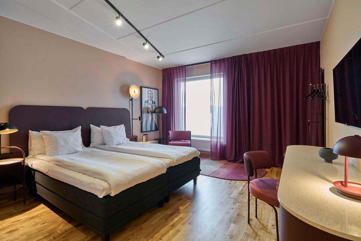 A modern hotel room with a large bed, a desk, and a chair.