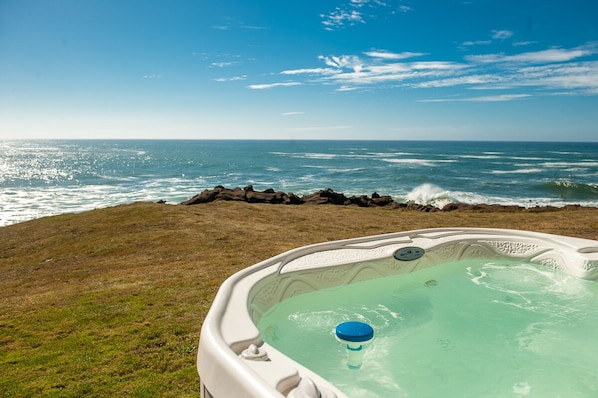 Relax in a hot tub overlooking the ocean, surrounded by a serene natural setting.